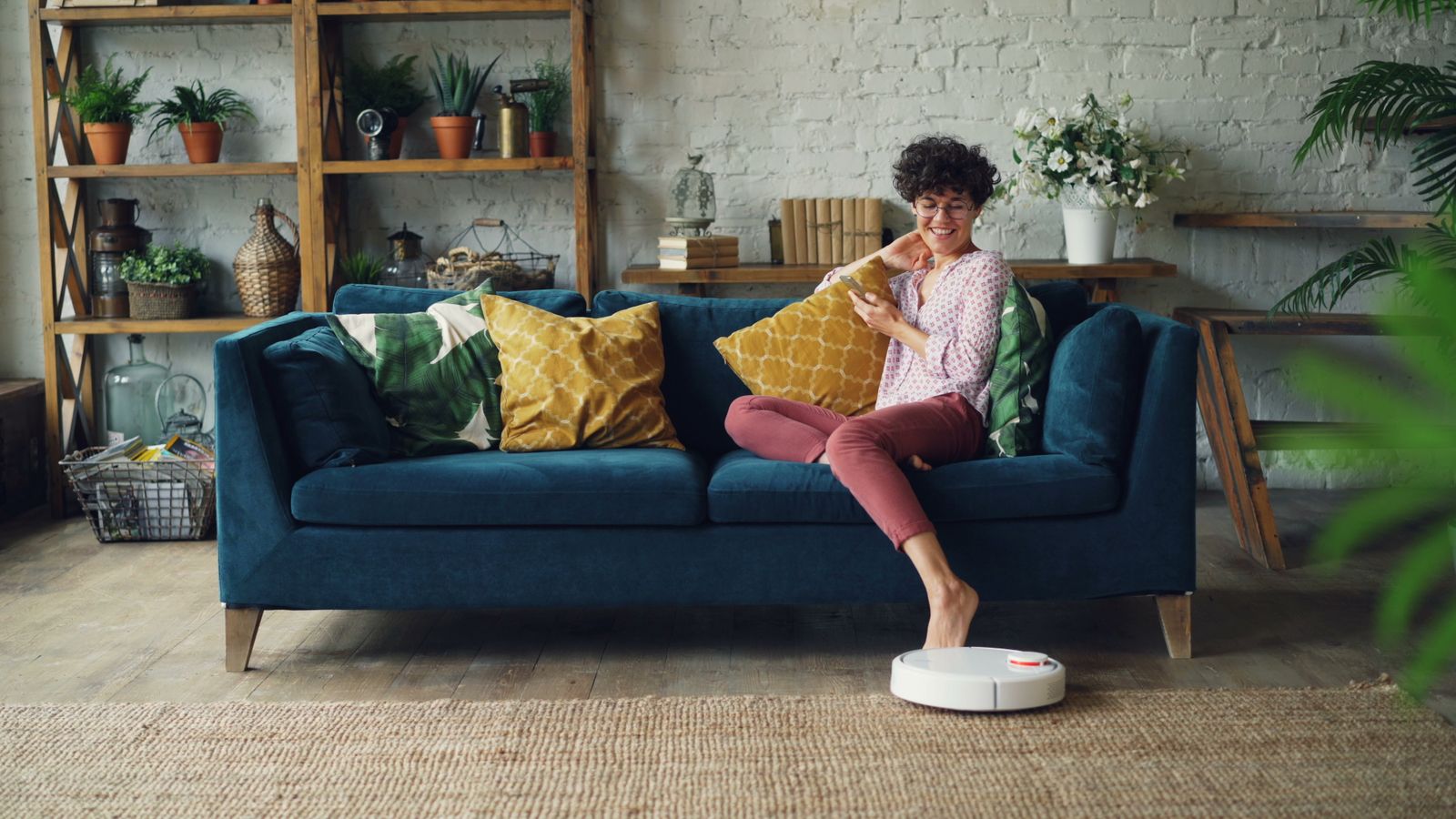 A robot cleaner at the edge of a rug in a living room while someone relaxes on the sofa