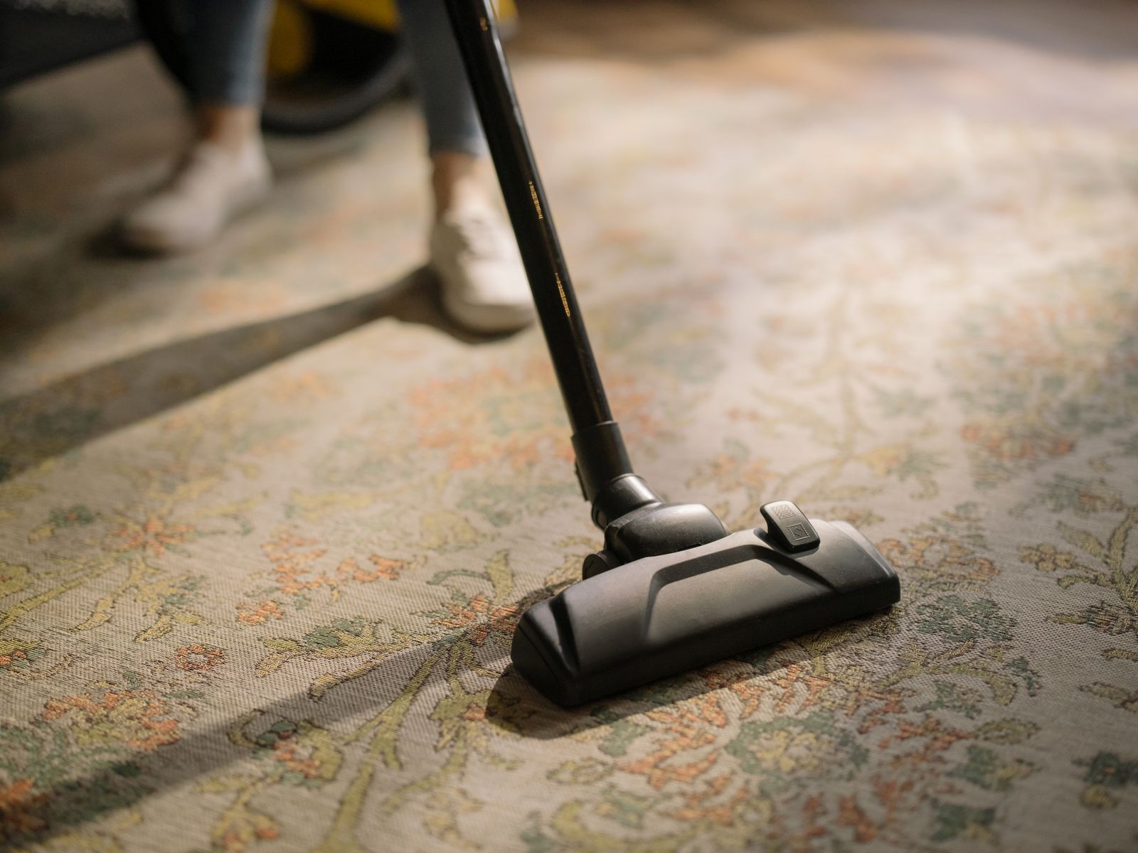 Close-up of an aged patterned carpet being cleaned in warm light